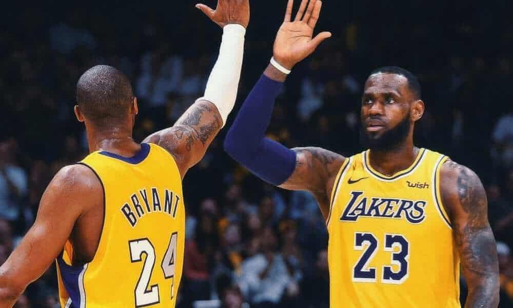 Kobe Bryant and Lebron James exchange a high-five while playing a basketball game wearing Lakers jerseys.
